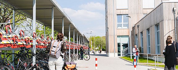 Fahrradparkhaus am Neubau der UW/H. Im Vordergrund steht eine Frau, mit dem Rücken zur Kamera, vor ihrem Fahrrad.