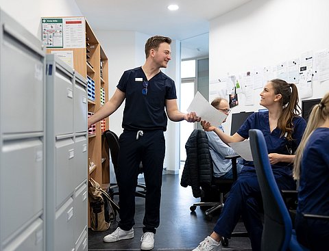 Studierende der Zahnmedizin beschäftigen sich mit administrativen Aufgaben, arbeiten an PCs und tauschen Dokumente aus.