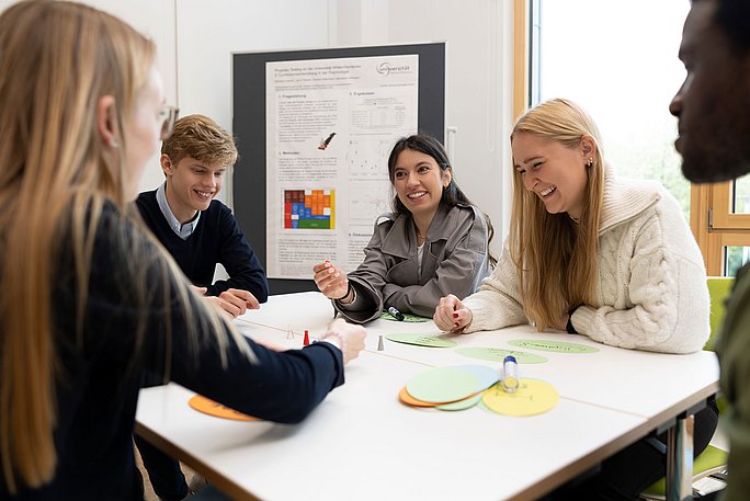 Studierende in enger Zusammenarbeit sitzen am Tisch.