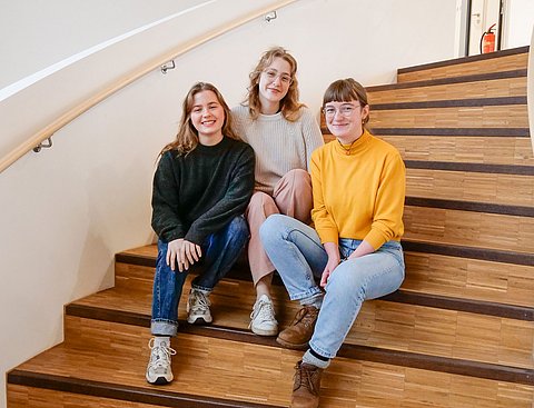 Ein Gruppenbild von drei Frauen, die auf einer Holztreppe sitzen.