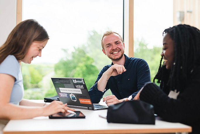 Zwei Studentinnen und ein Student sitzen im Lernflur und arbeiten zusammen am Laptop.