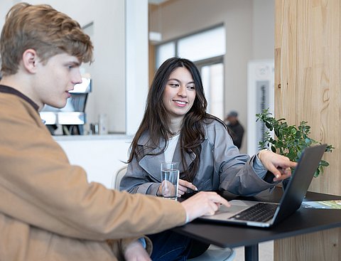 Eine junge Frau und ein junger Mann sitzen vor einem Laptop.