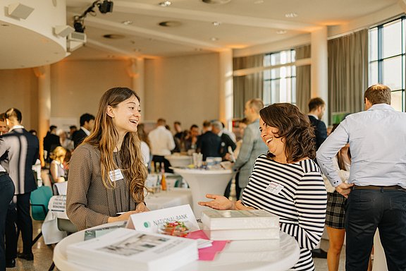 Foto von zwei Frauen, die an einem Stehtisch stehen und sich unterhalten.