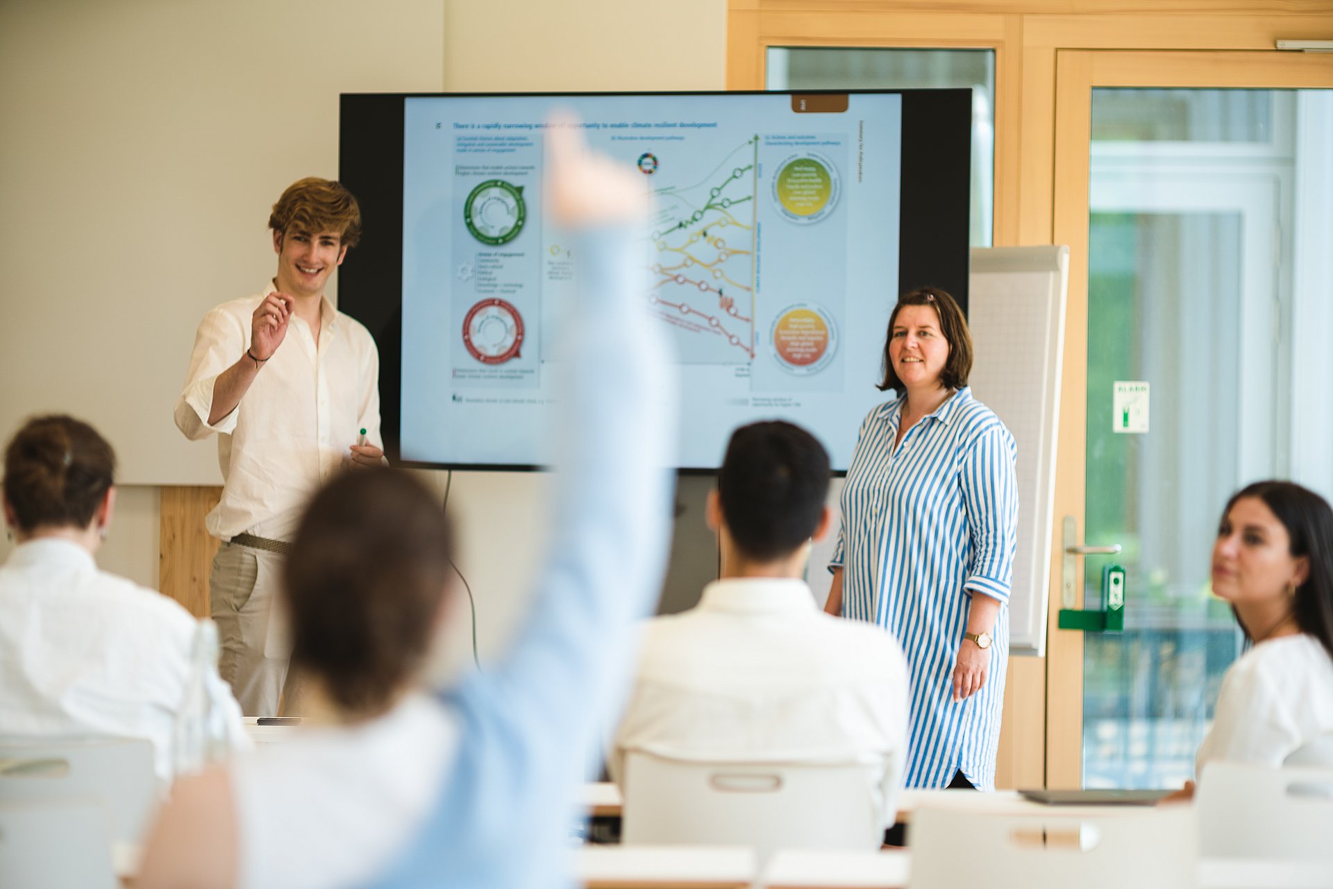 Lehrende und Studierende in einem Seminarraum mit Whiteboard