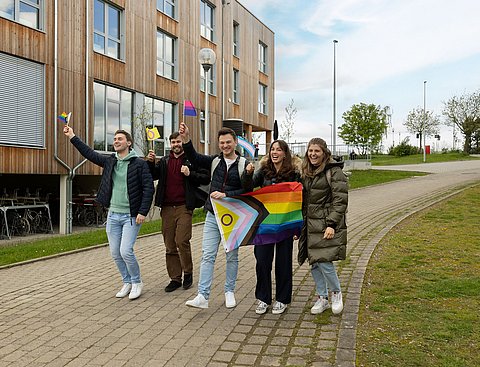 Eine Gruppe Studierender läuft mit geschwenkten Pride-Flaggen über dem Campus.