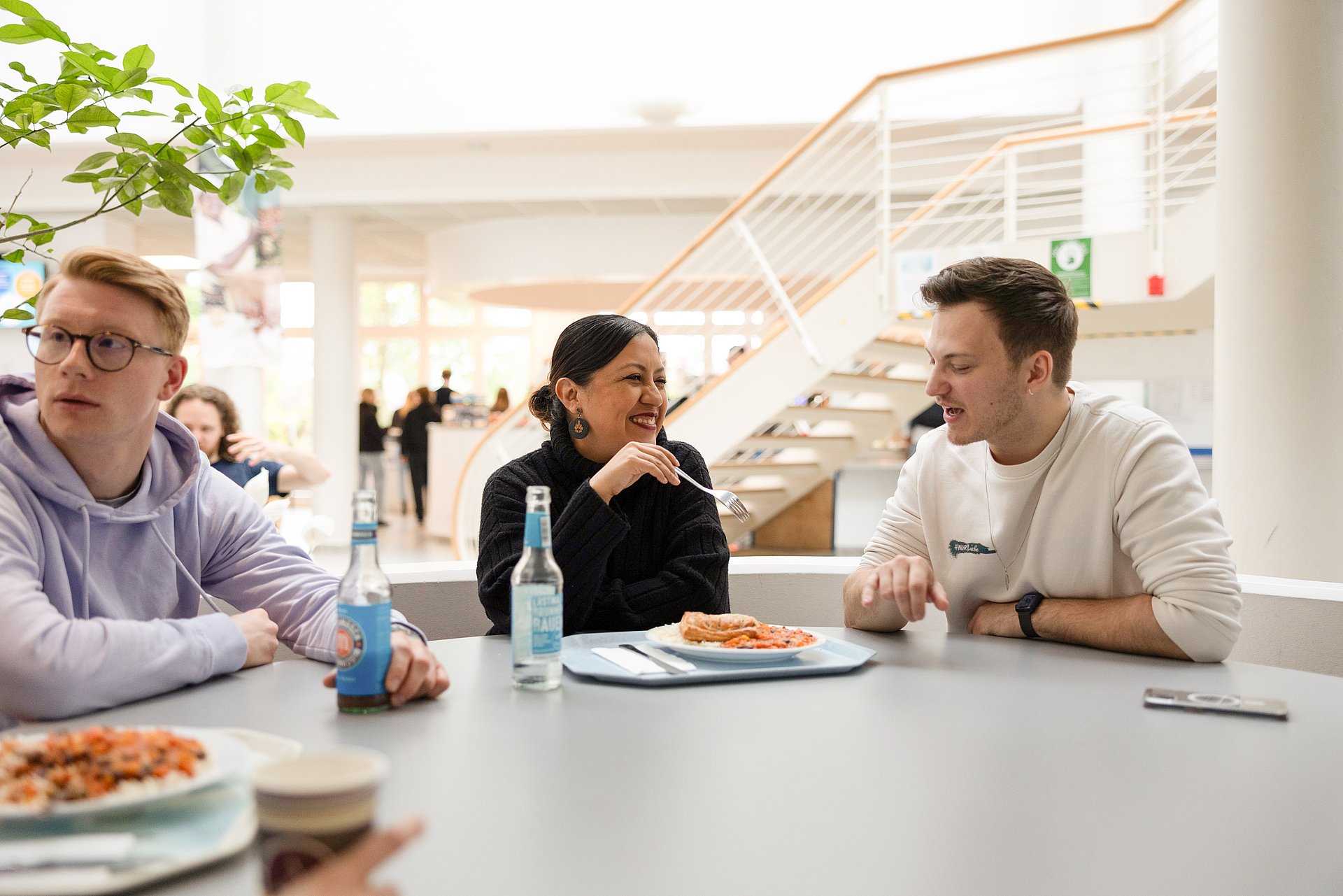 Drei Studierende sitzen an einem Tisch und essen zu Mittag.