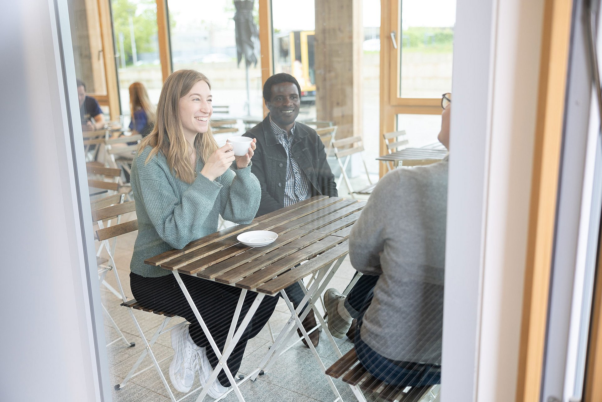 Three people are sitting at a table, drinking coffee and chatting.