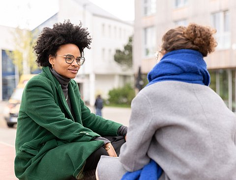 Zwei Studentinnen sitzen auf dem Campus der UW/H und sprechen miteinander.