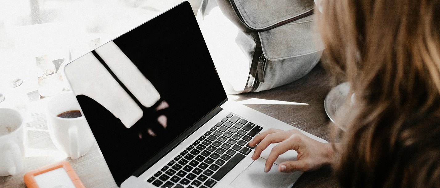 View over the shoulder of a woman sitting at a laptop.