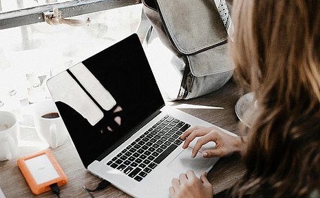 Blick über die Schulter einer Frau, die an einem Laptop sitzt.