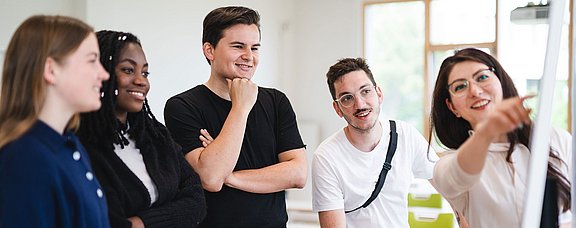 Gruppe von fünf Personen vor einem Whiteboard versammelt