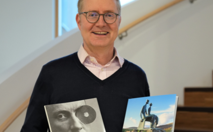 Portrait of a man. He is holding two art books in his hands.