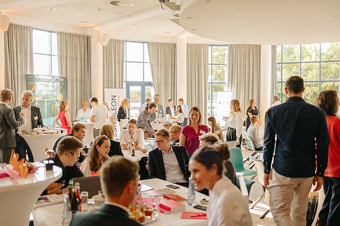 Veranstaltungsfoto: Ein festlich geschmückter Saal mit vielen Menschen in Gesprächssituationen.