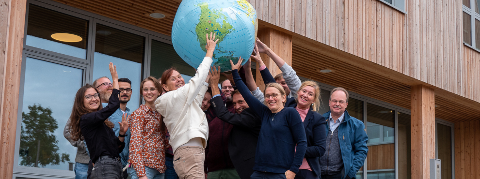 Many people hold an inflatable globe in the air together and smile at the camera.