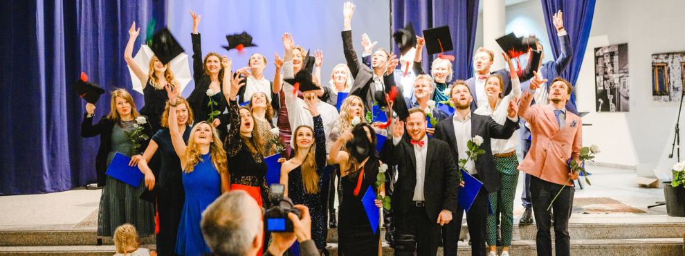 Graduates of Human Medicine at UW/H celebrate their graduation in festive attire. They have roses in their hands and throw up their graduation hats.