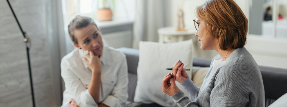 Zwei Frauen sitzen auf einer Couch und sind in ein Gespräch vertieft.