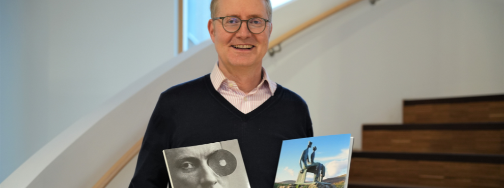 Portrait of a man. He is holding two art books in his hands.