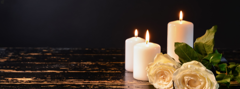 Three lit candles and two white roses against a dark background