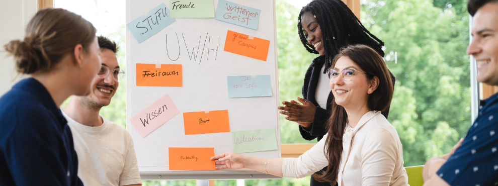 5 Studierende sitzen gemeinsam in einem Kursraum. In der Mitte ist eine Flipchart aufgebaut.