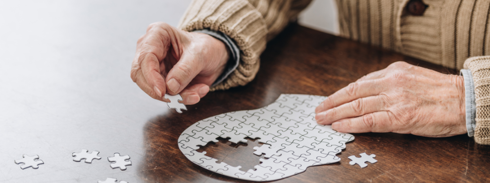 Hände einer älteren Person puzzeln einen Kopf zusammen als Symbolbild für Demenz